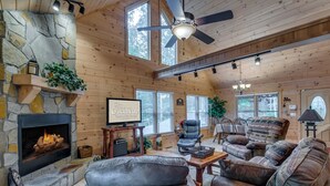 A cozy cabin interior with a stone fireplace, leather furniture, and large windows. - Country Dreams | Near Ocoee River | Hot Tub | Fire Pit (Copperhill)