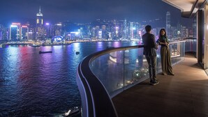 Un couple se tient sur un balcon, d’où l’on peut admirer la vue sur la ville illuminée la nuit.