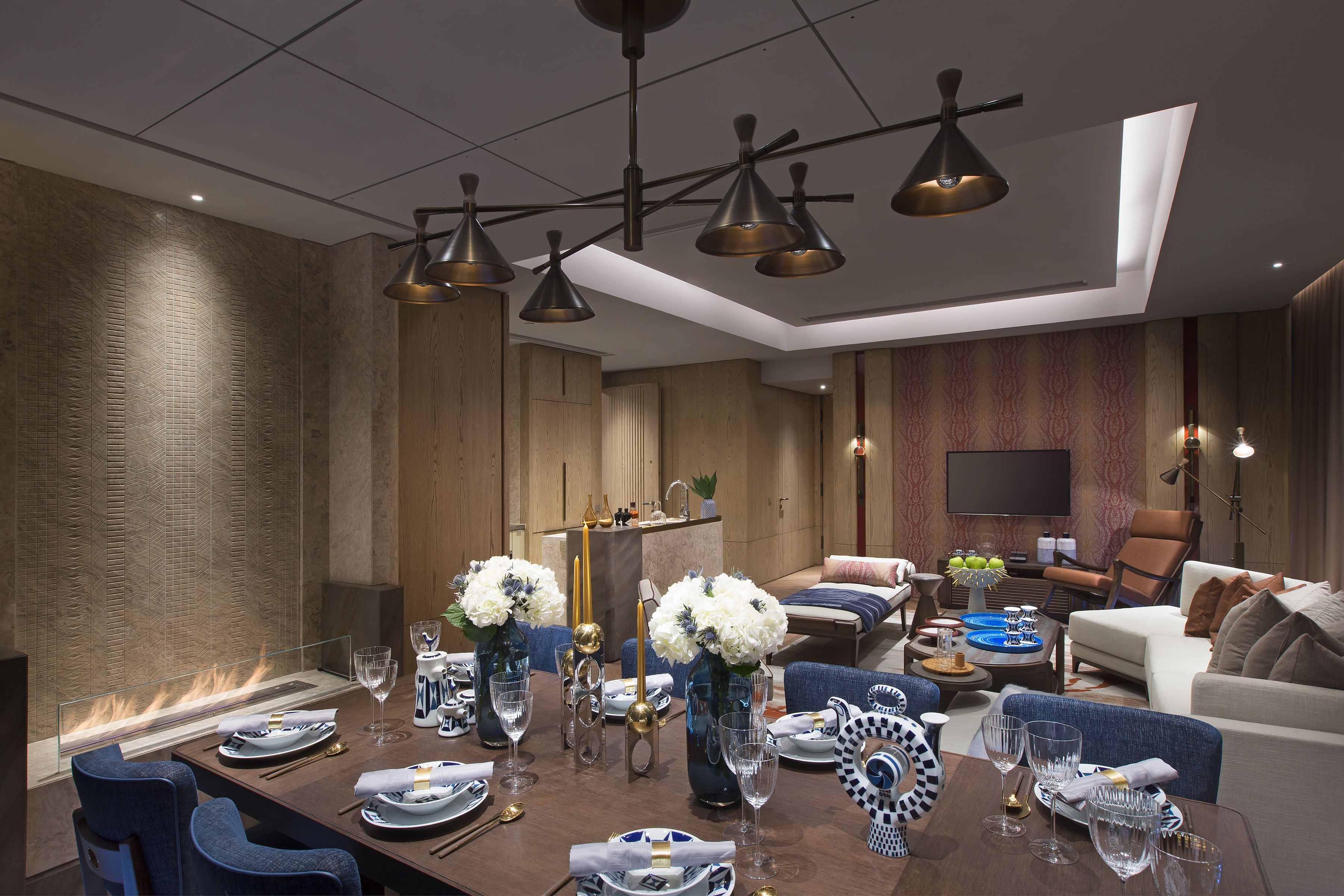 A modern dining area with a long table set for a meal, surrounded by sofas and a television.