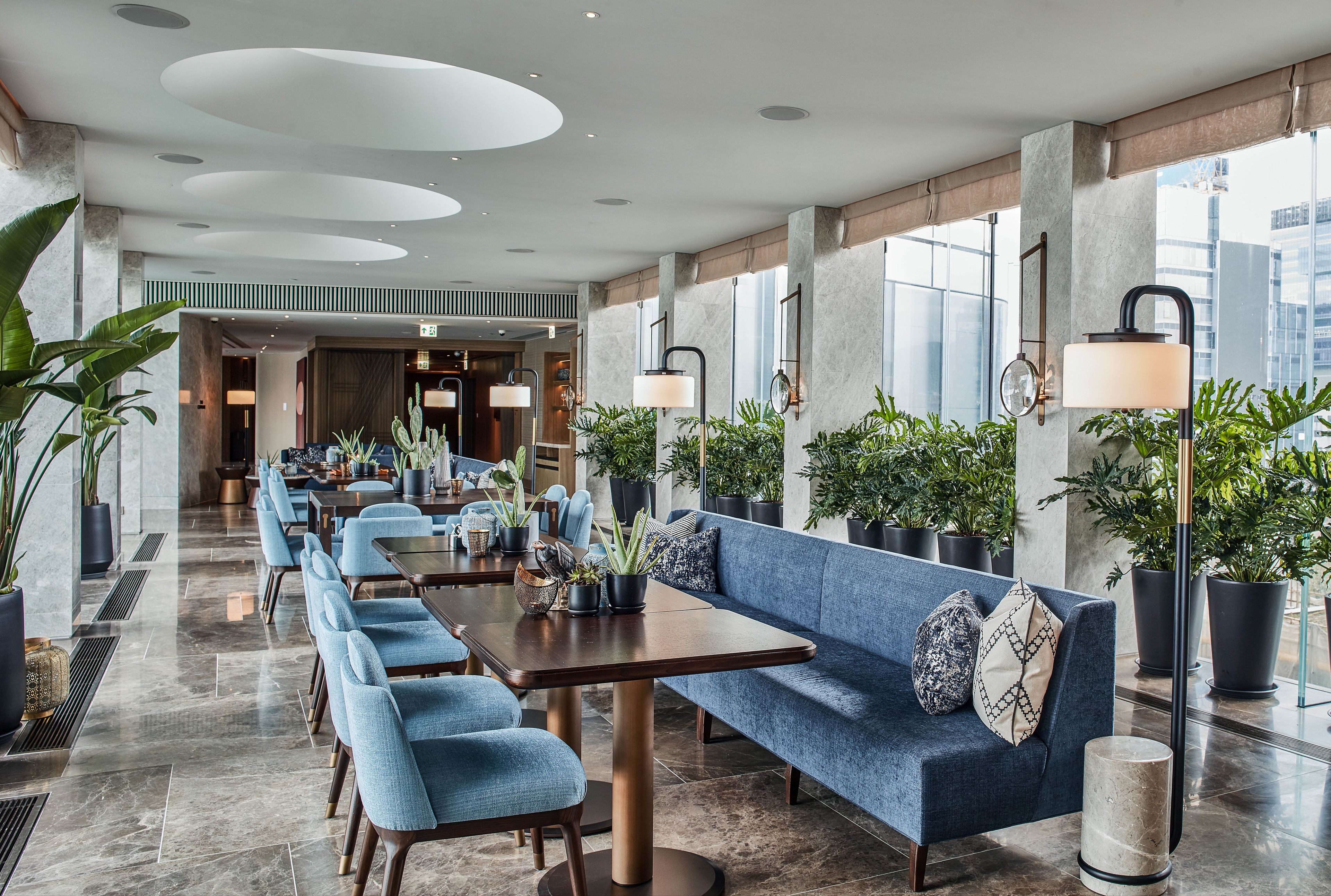 A modern hotel lobby with a long reception desk, blue seating, and potted plants.