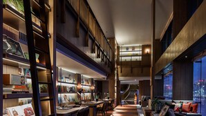 Un intérieur spacieux à plusieurs niveaux, doté de planchers en bois, d’un escalier central et d’un coin salon offrant une vue sur la ville.