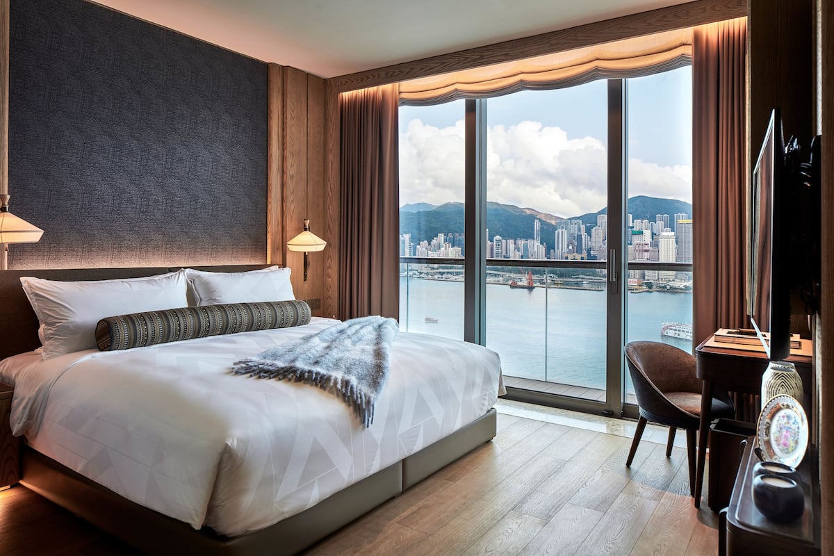 A hotel room with a large bed, a desk, and a view of a city skyline and water.