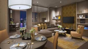 A modern living room with a sofa, chairs, a dining table set with plates and cutlery, a TV, and a bookshelf.
