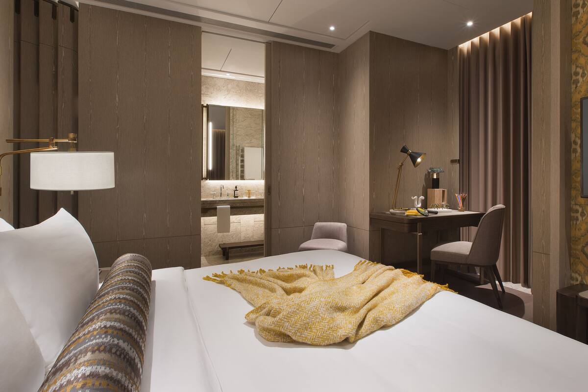 A hotel room with a large bed, a desk, a chair, a TV, and a bathroom visible through an open door.