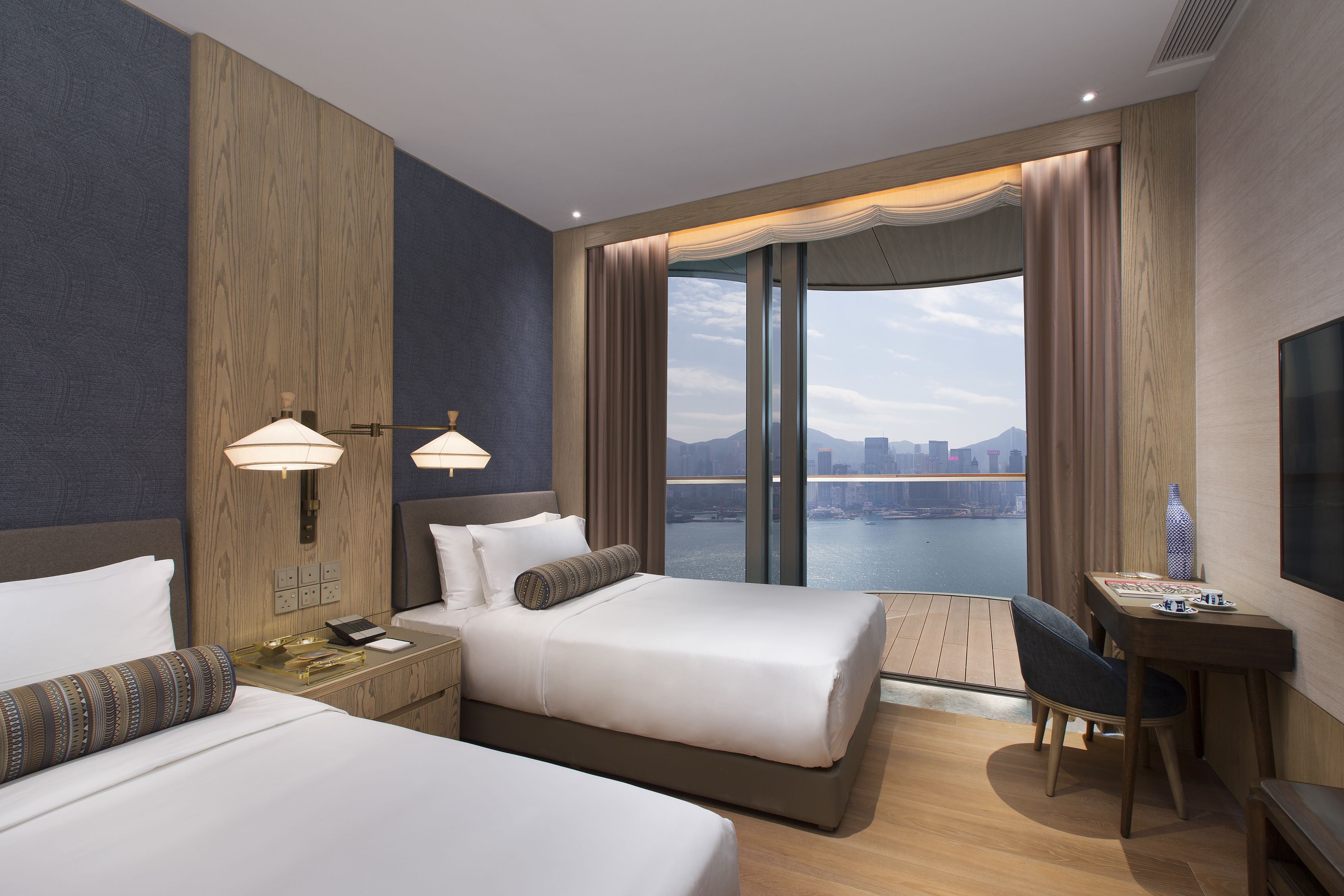 A hotel room with two beds, a desk, and a view of a cityscape.
