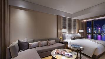 A modern hotel room with a sofa, a bed, a nightstand, and a view of the cityscape at night.