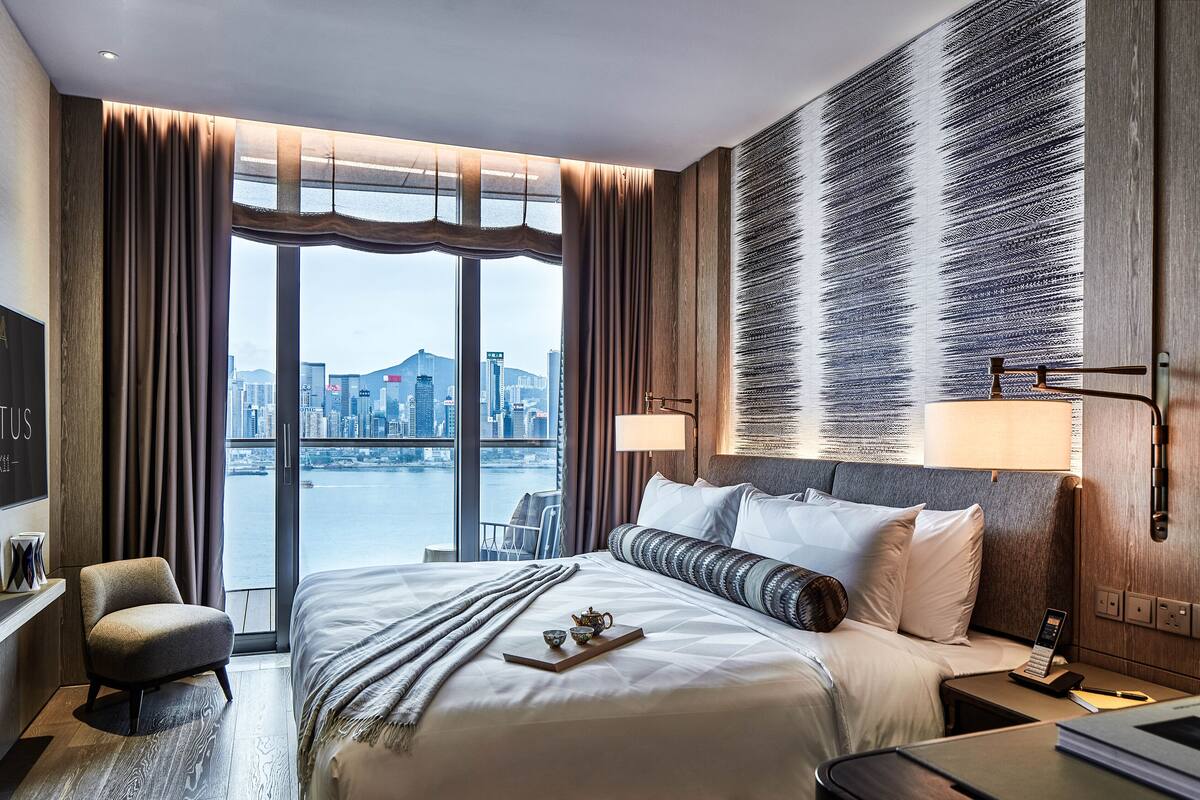 A modern hotel room with a large bed, a view of the city, and a cityscape visible through the window.