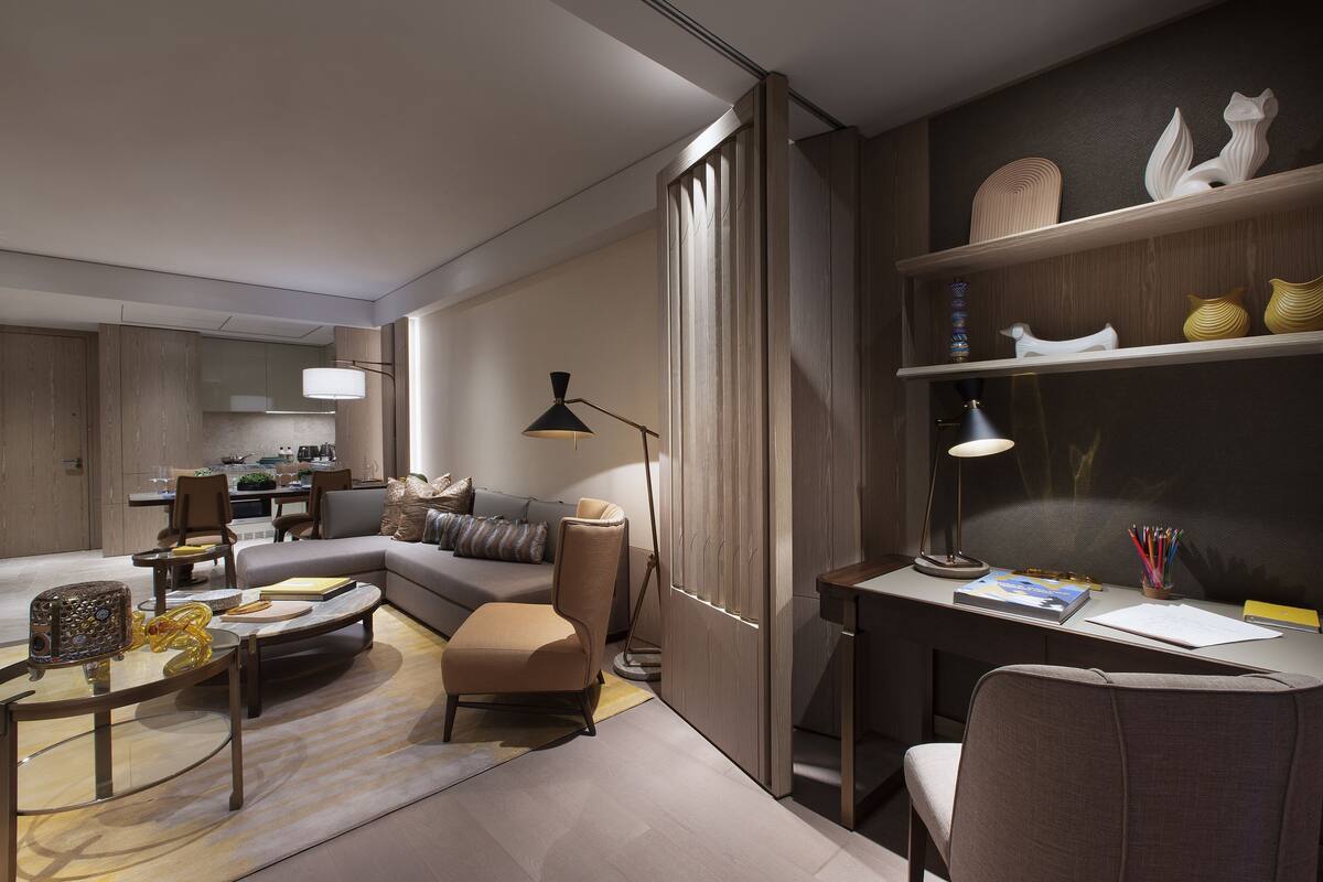 A modern living room with a sofa, coffee table, and a desk with a lamp and books.