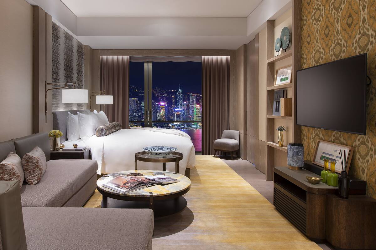 A hotel room with a bed, sofa, TV, and a city view.