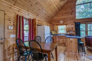A wooden cabin with a kitchen area, dining table, and chairs. - Treetops | Hot Tub | Fire Pit | Pool Table (Copperhill)