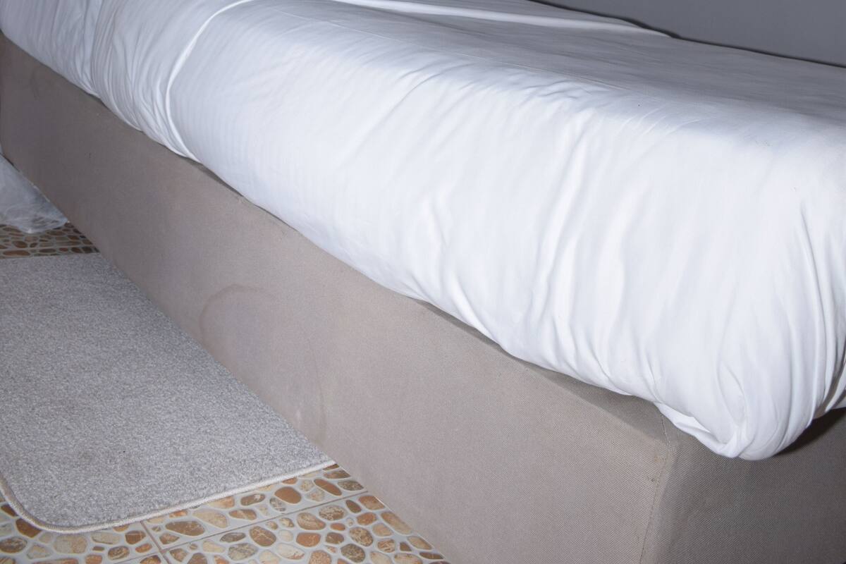 Una cama con ropa blanca, una almohada azul y un cabecero gris.