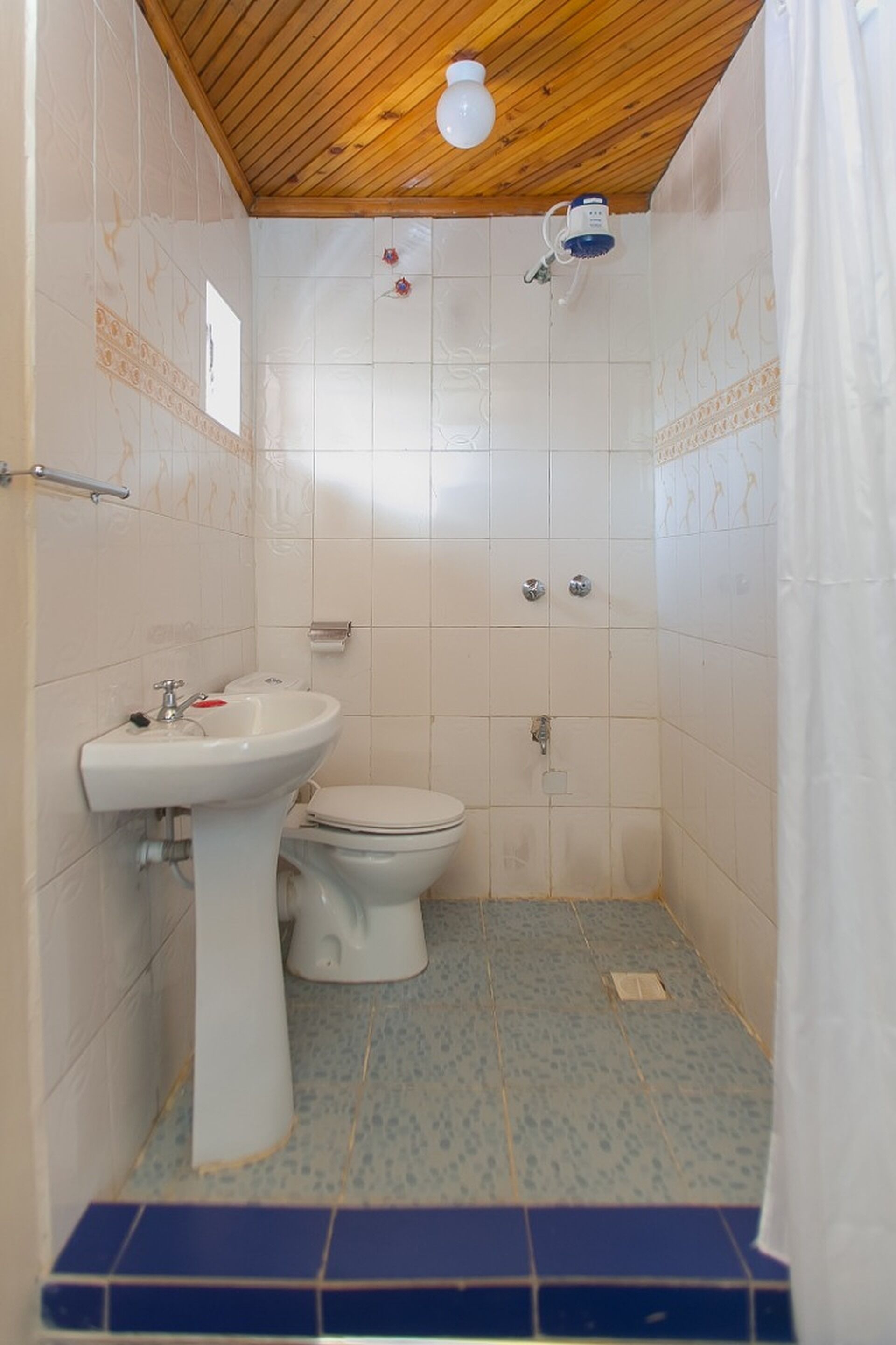 Un baño pequeño con techo de madera, un lavabo blanco, un inodoro y una zona de ducha.