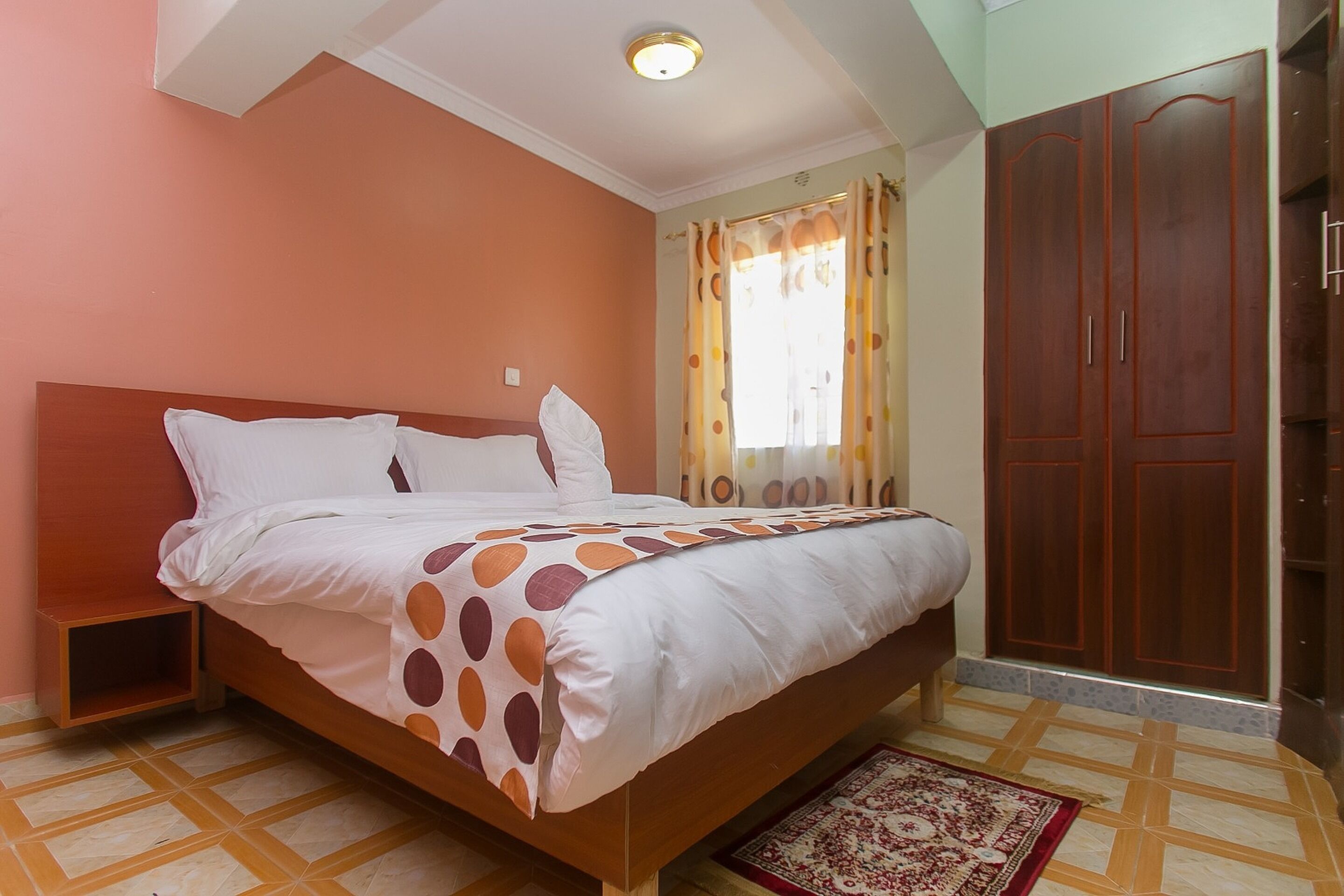 Un dormitorio con cama, mesita de noche, armario y ventana con cortinas.