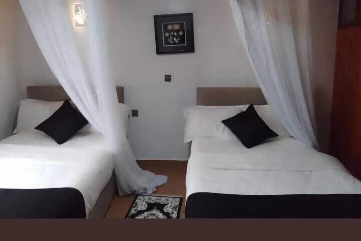 Una habitación con dos camas, cada una con ropa blanca y almohadas negras, separadas por un pequeño tapete.