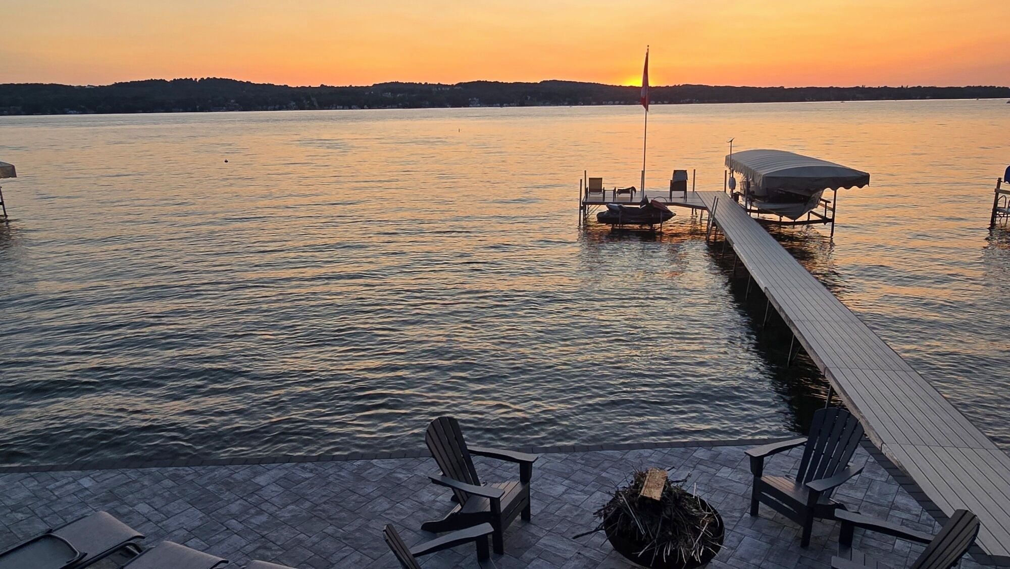 A lakeside dock with chairs and a covered area, overlooking calm water.