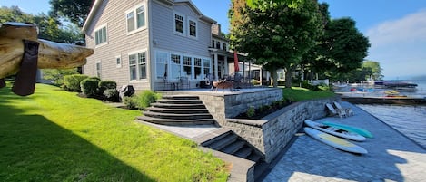 A two-story house with a patio, steps leading to a deck, and a view of boats on the water.
