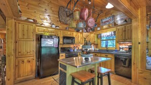 A wooden cabin kitchen with a central island, wooden cabinets, a refrigerator, microwave, stove, and hanging pots.