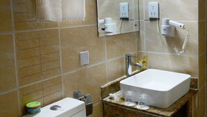 Een badkamer met toilet, wastafel en spiegel. Handdoeken hangen aan een rek, er staat een prullenbak bij de wastafel en een zeepdispenser.