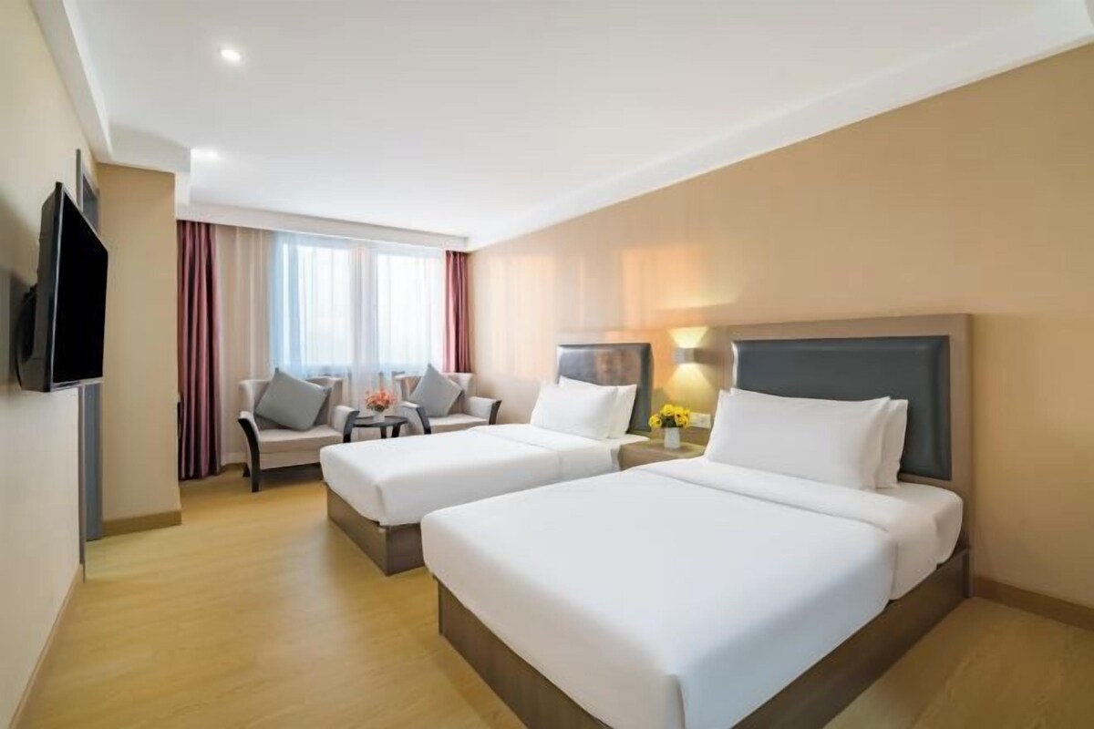 A hotel room with two beds, a TV, a desk, and a chair.