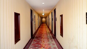 Een hotelgang met een kamerbreed tapijt, houten deuren en een plafond met inbouwspots.