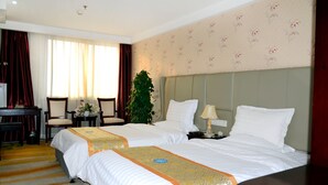 Een hotelkamer met twee bedden, een bureau, stoelen, een plant en een raam met gordijnen.