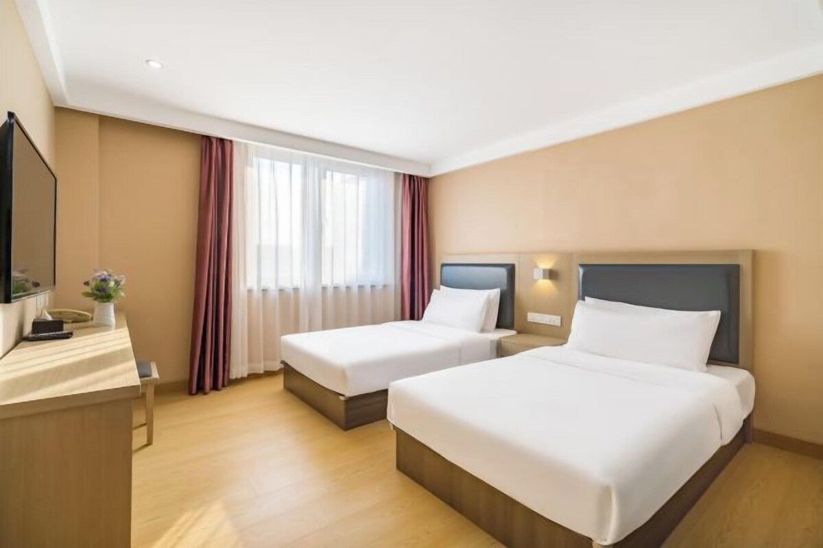A hotel room with two beds, a desk, and a TV.