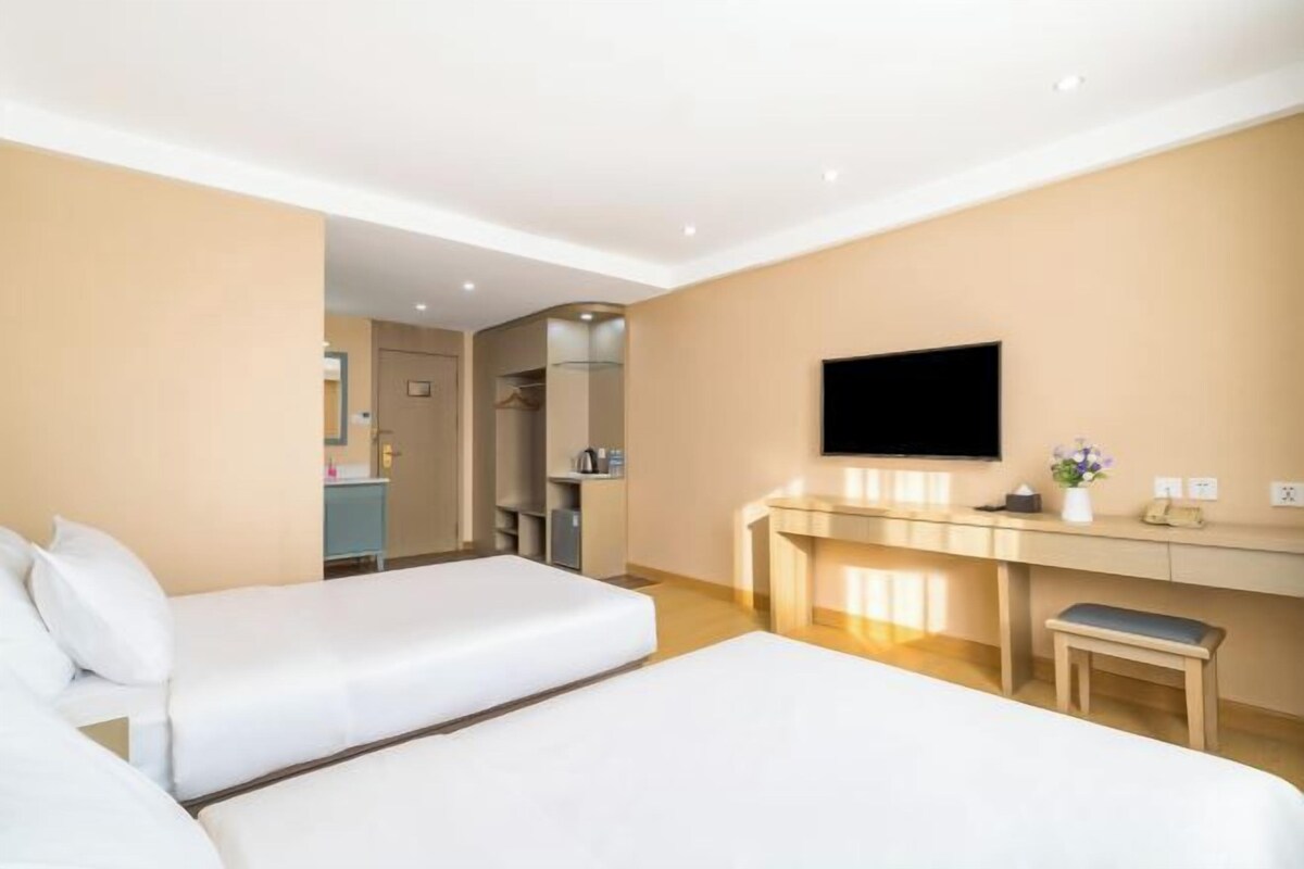A hotel room with two beds, a desk, a TV, and a kitchenette.