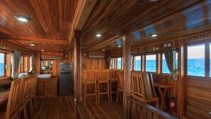 Une cabane avec un intérieur en bois, un coin cuisine et de grandes fenêtres offrant une vue sur l’océan.