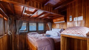 Une cabine aux murs en bois, avec un lit superposé, une fenêtre avec des rideaux et une vue sur l’eau.