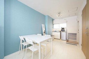 A modern kitchen with white appliances, a dining area with white chairs, and a blue accent wall.