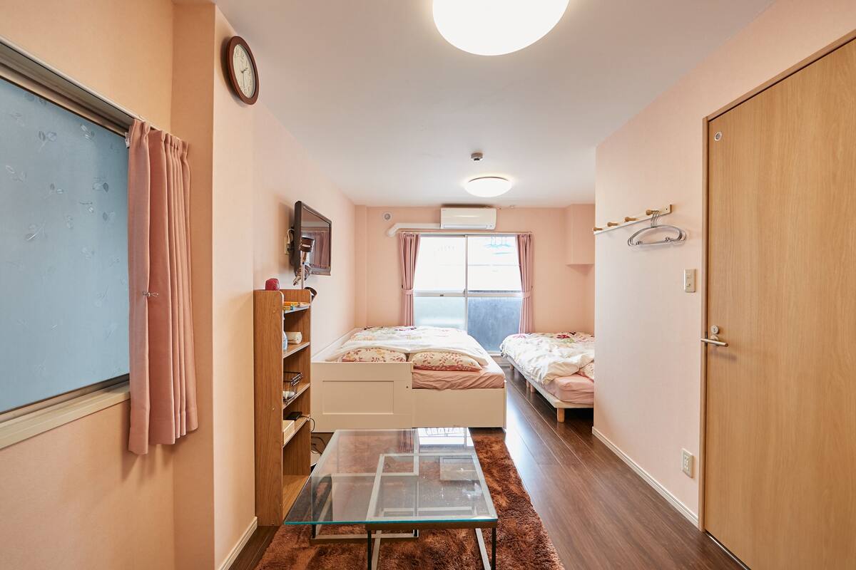 A bedroom with two beds, a glass table, a wardrobe, and a window with curtains.