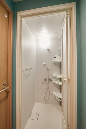 A small, enclosed shower area with a white door, a glass shower enclosure, and a white shelf with toiletries.