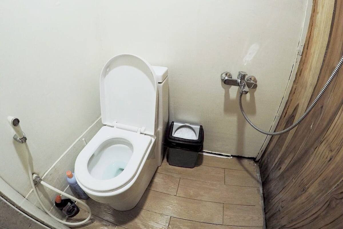 A small, compact bathroom with a toilet, a trash bin, and a shower.