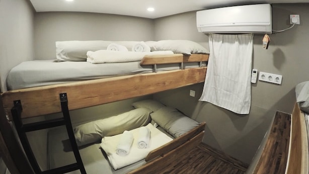 Une chambre avec un lit superposé, un ventilateur de plafond, une petite commode en bois et un climatiseur fixé au mur.
