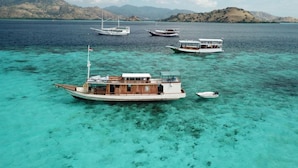 Un bateau doté d’une cabine et d’un espace sur le pont, entouré d’une eau turquoise cristalline et de collines lointaines.