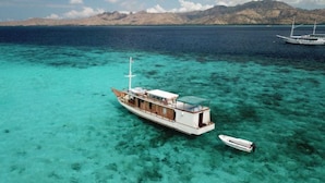 Un bateau doté d’une cabine et un plus petit bateau amarrés à proximité, le tout entouré d’une eau turquoise cristalline et de montagnes lointaines.