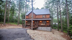 A two-story log cabin with a stone foundation, surrounded by a forest. - Cowboy Castle - Ridge Line Lodge, Hot Tub, Games, Outdoor Entertaining🔥 🌲 (Broken Bow)