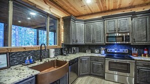 A modern kitchen with granite countertops, stainless steel appliances, and dark wood cabinets. - Cowboy Castle - Ridge Line Lodge, Hot Tub, Games, Outdoor Entertaining🔥 🌲 (Broken Bow)