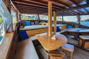A wooden deck with seating areas, including a bench and a table with a vase of flowers.