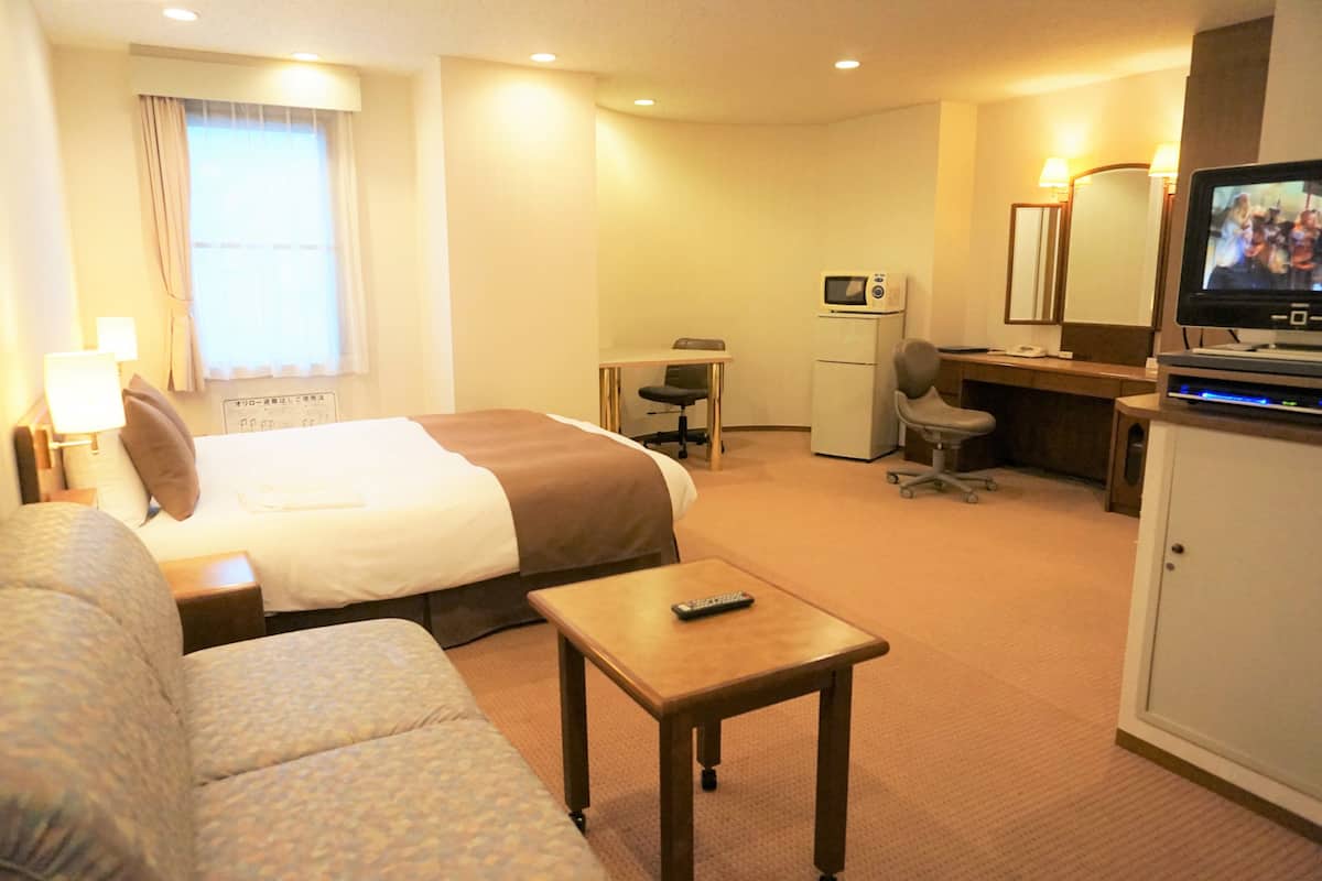 A hotel room with a bed, a small desk with a chair, a television, a microwave, and a cabinet.