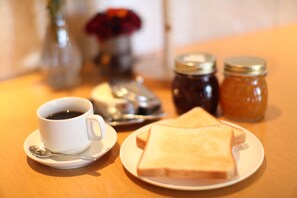 A breakfast setting with a cup of coffee, a plate of toast, and two jars of jam on a wooden table. - Hotel Yokosuka (Yokosuka)