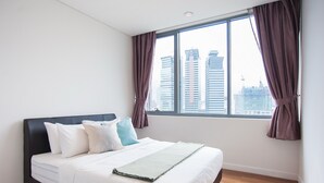 A modern hotel room with a large bed, white bedding, and a view of tall buildings through a window with purple curtains. - S8 COZY 1 BR - KLCC - KL Tower - High Speed WiFi (Kuala Lumpur)