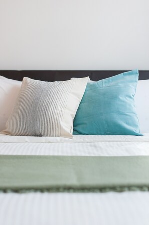 A bed with two pillows, one striped and one solid teal, against a dark headboard. - S8 COZY 1 BR - KLCC - KL Tower - High Speed WiFi (Kuala Lumpur)