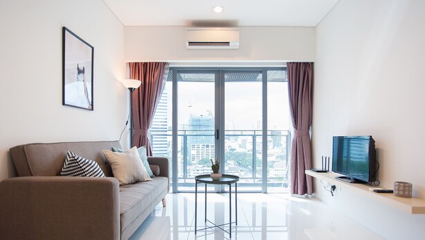 A modern living room with a sofa, a small round table, a flat-screen TV, and a large window with curtains. - S8 COZY 1 BR - KLCC - KL Tower - High Speed WiFi (Kuala Lumpur)