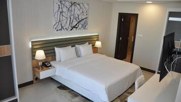 A modern hotel room with a large bed, bedside lamps, a flat-screen TV, and a wall-mounted artwork.