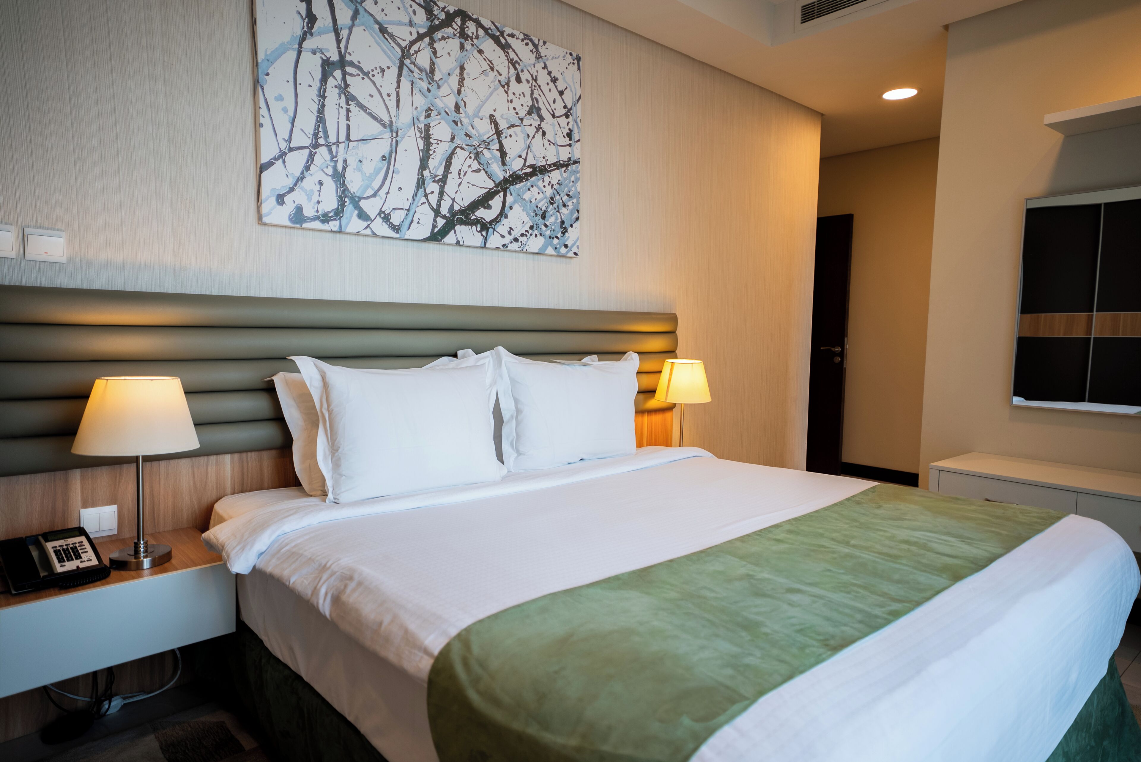 Habitación de hotel con una cama grande, dos lámparas de noche, un teléfono y un cuadro colgado en la pared.