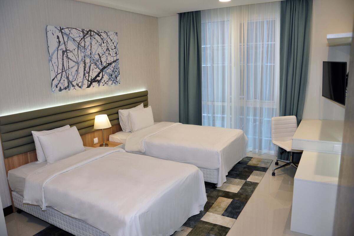 A hotel room with two beds, a desk, a TV, and a large abstract painting on the wall.