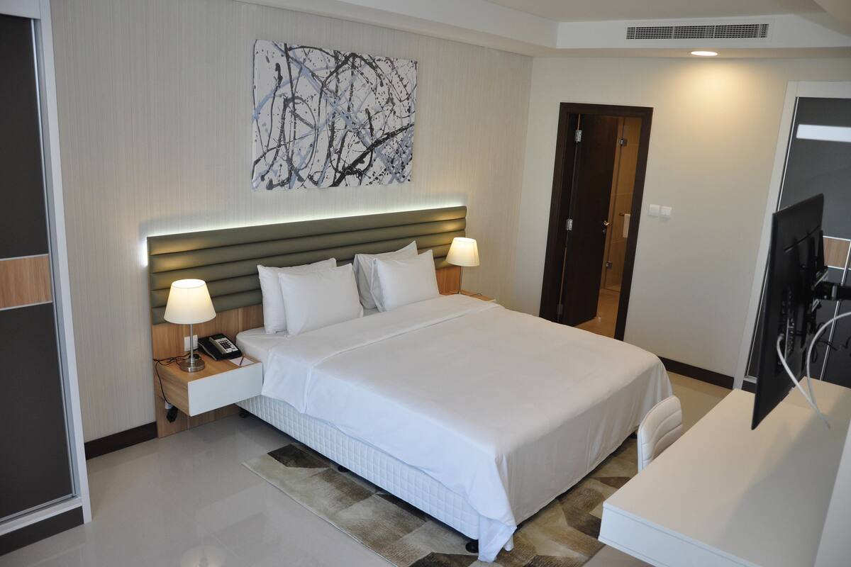 A hotel room with a large bed, bedside lamps, a flat-screen TV, and a wall art piece.