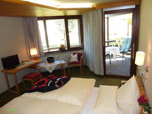 Ett hotellrum med en säng, ett skrivbord med en dator, en stol, ett bord med en lampa och utsikt över omgivningarna.