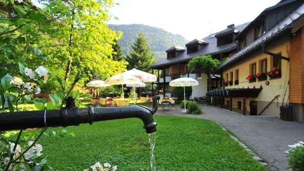Un jardin avec une fontaine, un bâtiment doté d’une terrasse, et une montagne en arrière-plan.